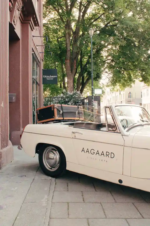 A beautiful vintage car with some luggage displayed in the trunk, parked in the sideway with a tree in the background